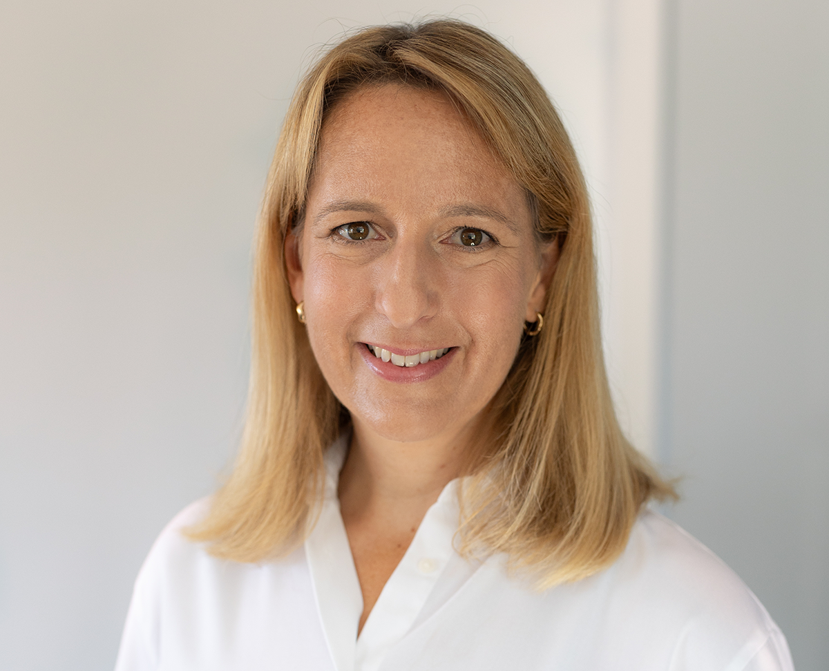 Frau Dr. Carolus. Lächelnde Frau mit langen blonden Haaren in einem hellen Raum. 