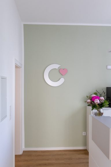 Wand mit grüner Farbe, runder Dekoration in Weiß und Pink sowie frischen Blumen auf einer Fläche.